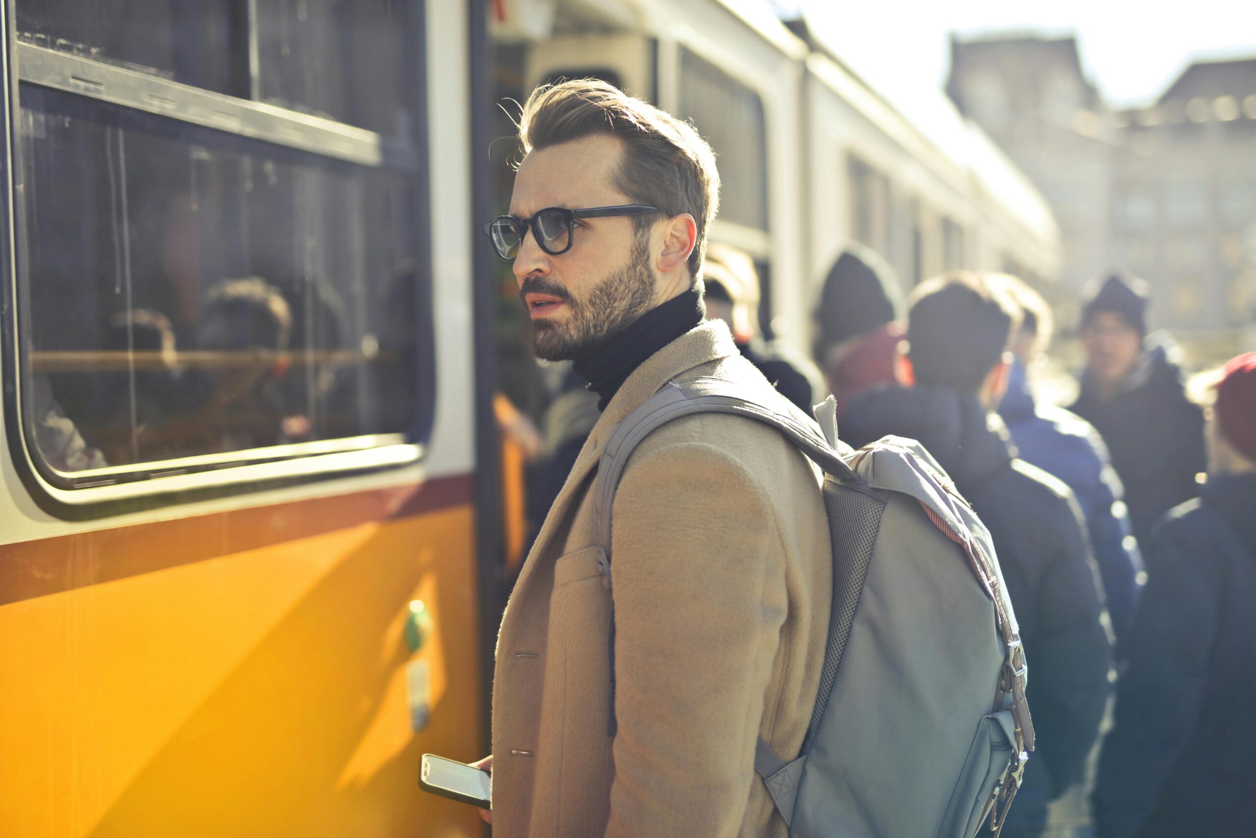 A stylish man with a backpack boards a tram in bustling Budapest, Hungary, during the day.